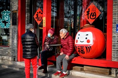 Varias personas mayores conversan en el exterior de un restaurante en una calle de Pekín. 