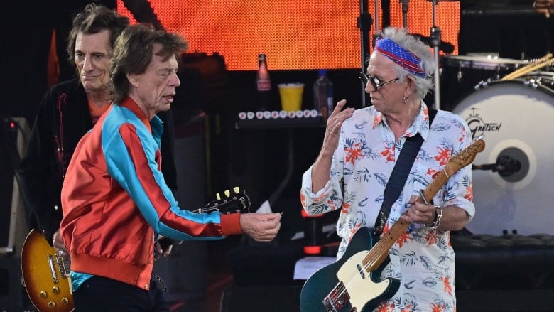 Three men are shown performing on stage, with two holding guitars.