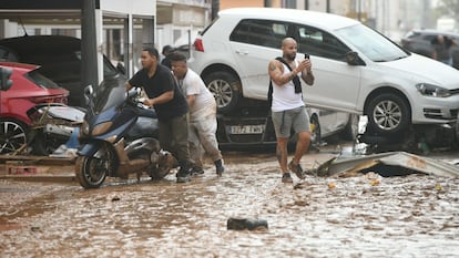Varias personas trasladan una motocicleta en una calle inundada en el barrio de La Torre en Valencia, este miércoles.