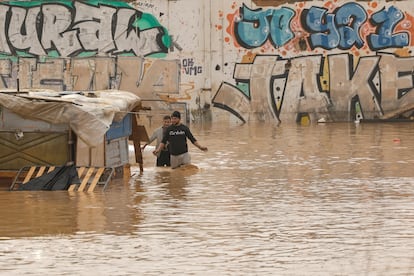Dos personas vadean un terreno de chabolas inundado junto a la V-30 en Valencia, este miércoles.