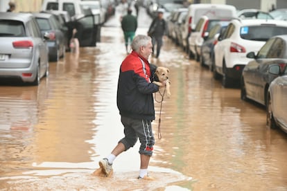 Un hombre sujeta a su perro mientras camina por una calle inundada en Xirivella (Valencia), este miércoles.