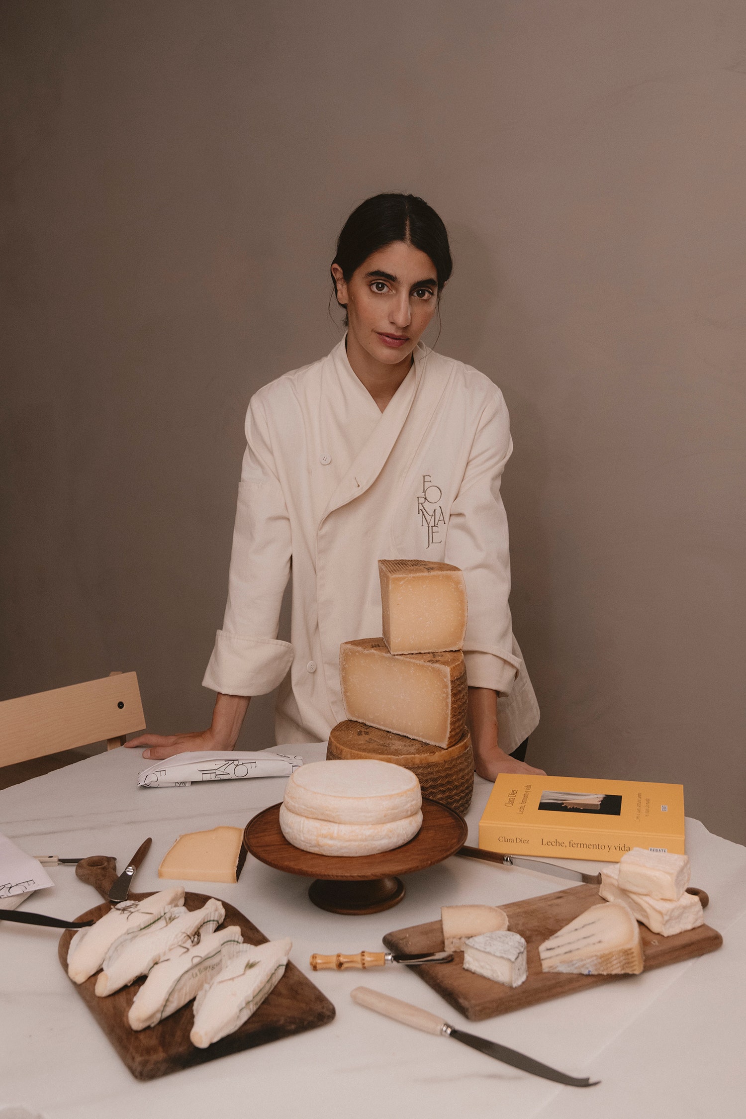 Clara con su propio uniforme y junto a su libro  preparando una tabla de quesos.