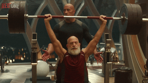 Santa Claus cargando una pesa enorme para demostrar lo fuerte que s necesita ser para entregar todos los regalos alrededor del mundo en la historia de Código: Traje rojo.- Blog Hola Telcel 