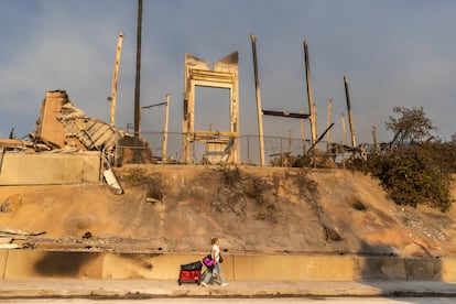 Una mujer que lleva algunas de las pertenencias que ha sacado de su casa, pasa por debajo de los restos de una iglesia luterana quemada tras el  incendio de Pacific Palisades, en Los Ángeles.