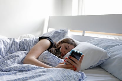 Una adolescente acostada en la cama mirando su teléfono móvil.