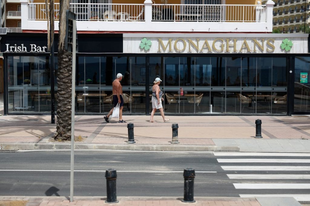 Dos personas pasean por la puerta del bar donde murieron a tiros dos escoceses en Fuengirola, antes de que retiraran el rótulo.