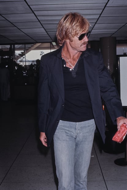 'Famoso en aeropuerto' es uno de los subgéneros que mejor definen la celebridad. ¿Cómo viajan las estrellas? Robert Redford proponía, en esta imagen de 1980, el mejor antídoto contra el hoy omnipresente chándal.