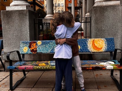 Dos alumnos del CEIP Rufino Blanco, en Madrid, se abrazan junto a un banco decorado.