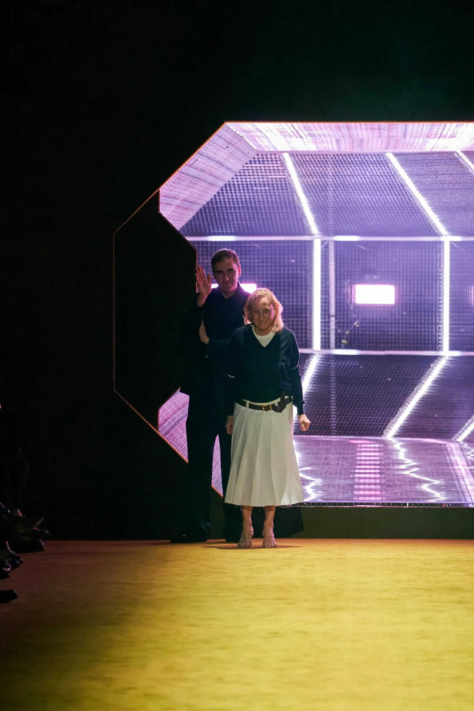 Image may contain Raf Simons Miuccia Prada Lighting Clothing Skirt Architecture Building Outdoors Shelter and Face