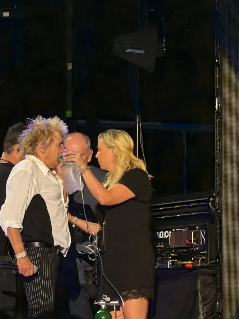 Rod Stewart receiving oxygen from a crew member during a concert.
